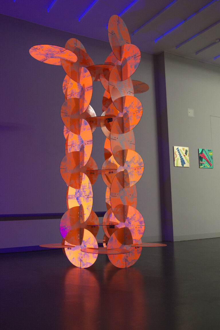 Orange geometric sculpture in a gallery setting.