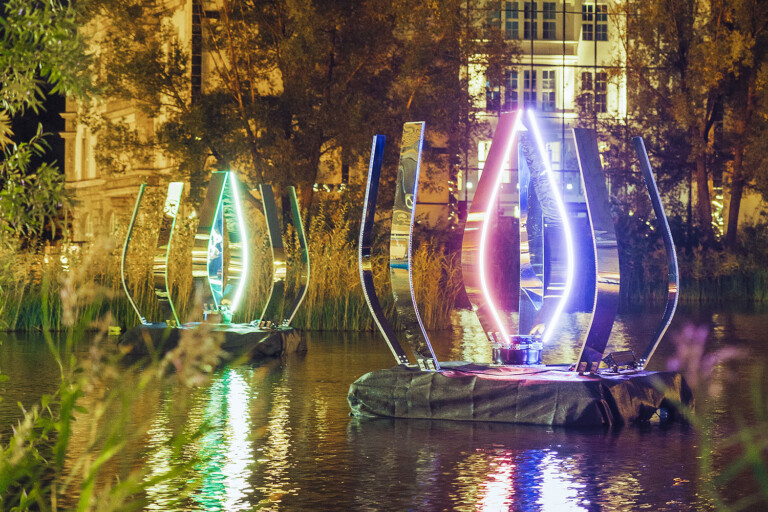 Illuminated sculptures reflecting in a pond at night.