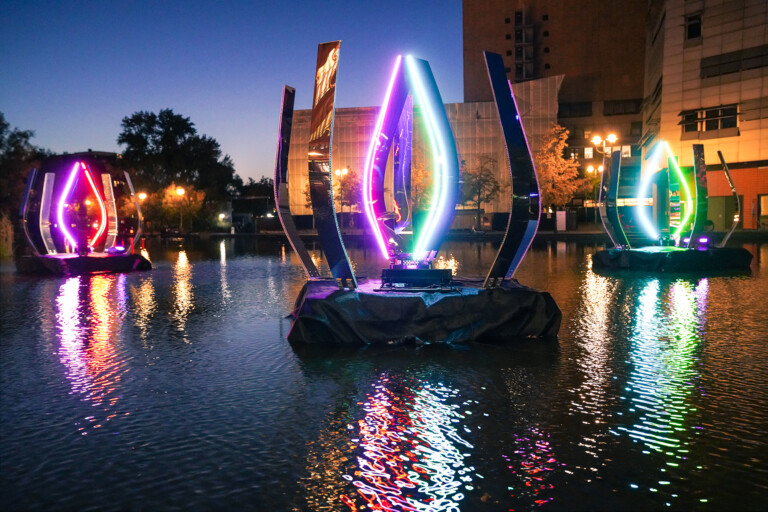 Colorful illuminated outdoor art installations on water at dusk.
