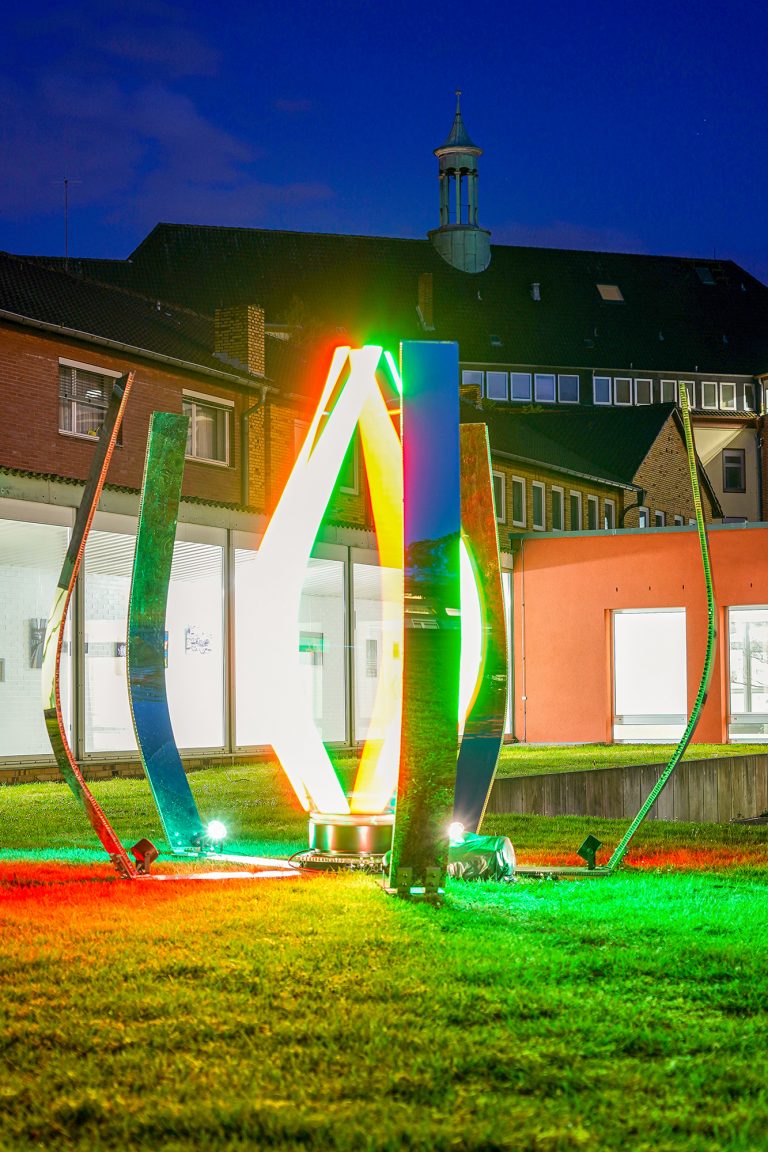 Colorful illuminated sculpture on grass at night.