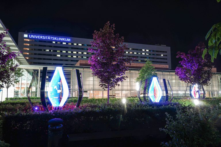 Universitätsklinikum building illuminated at night with sculptures.