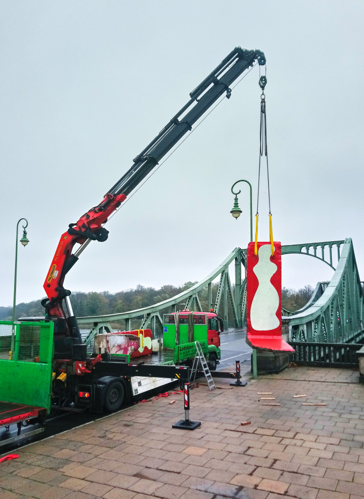 Crane lifting sculpture near a bridge