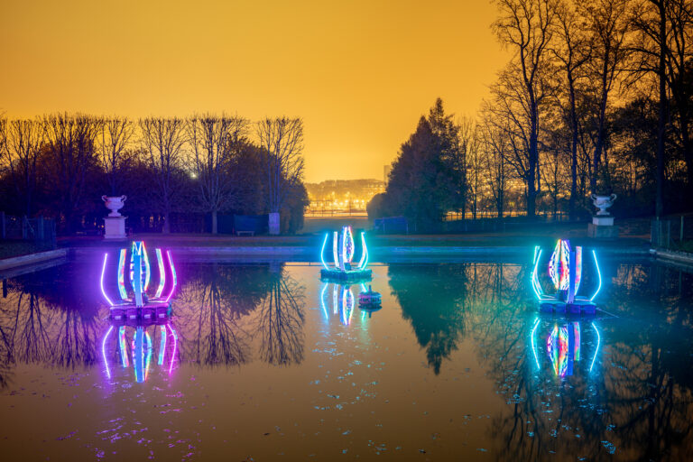 Colorful light installations on illuminated pond at dusk.